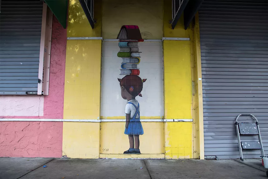 a mural depicts a young Black girl balancing books on her head