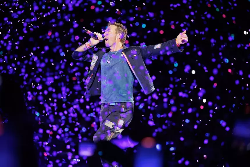 Coldplay singer on stage wearing a blue shirt and pants.