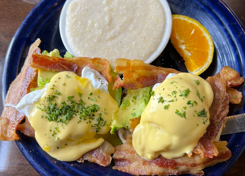 eggs Benedict on a blue plate with bacon and side of grits
