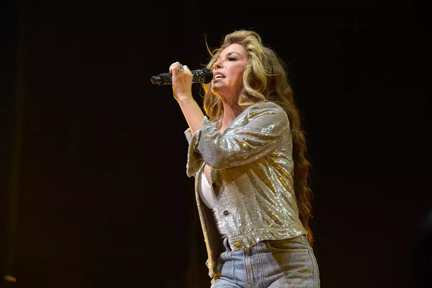 Blonde woman singing on stage holding a microphone.
