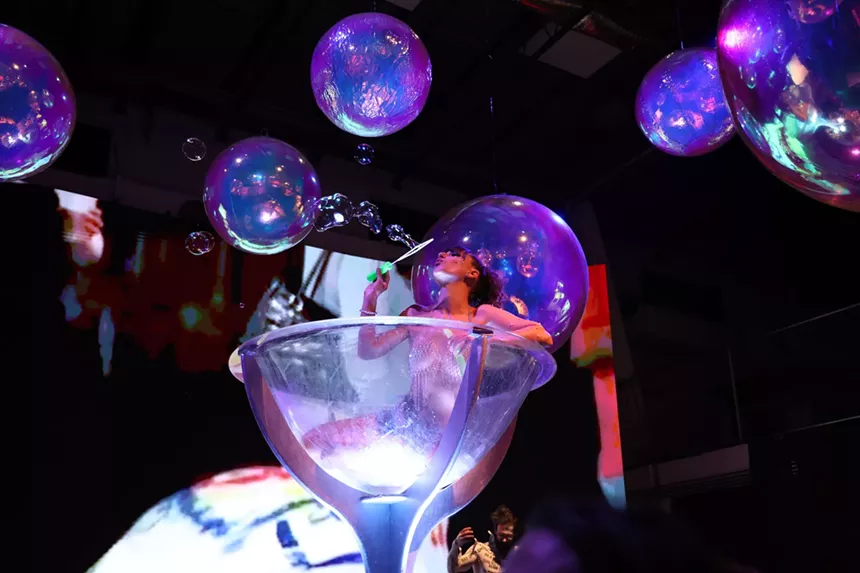 a burlesque dance blowing bubbles inside a human-sized martini glass