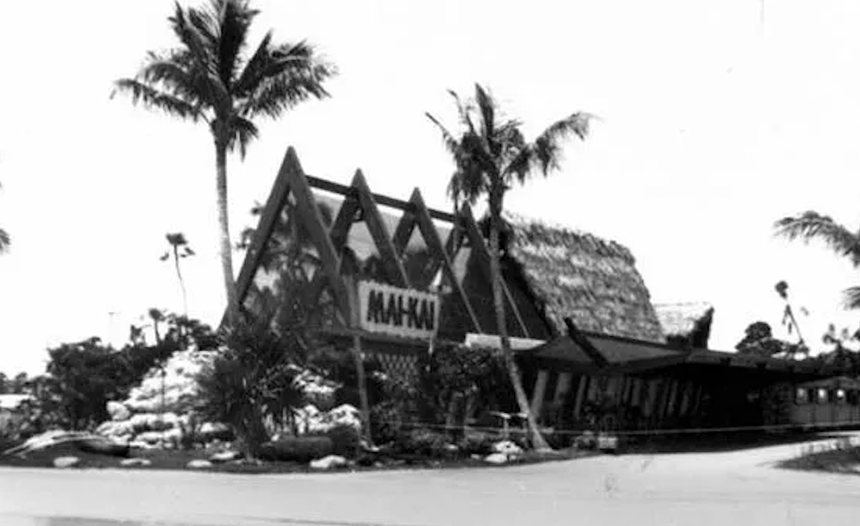 a black and white photograph of an old A-structured building with palm trees surounding it