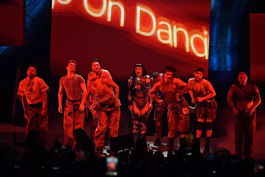 a performer and a group of dancers on stage, lit with red lights.