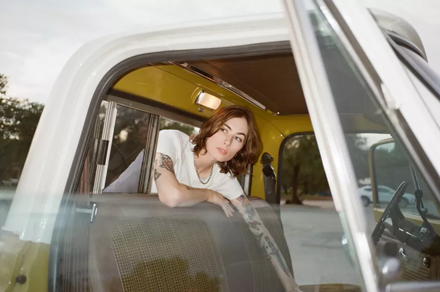 musician Claire Rousay sits in the back of a truck with her upper body through the back window to access the front seat