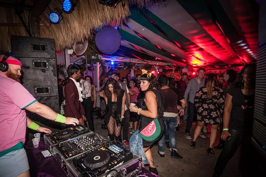 a crowd dances on a dance floor in front of a DJ