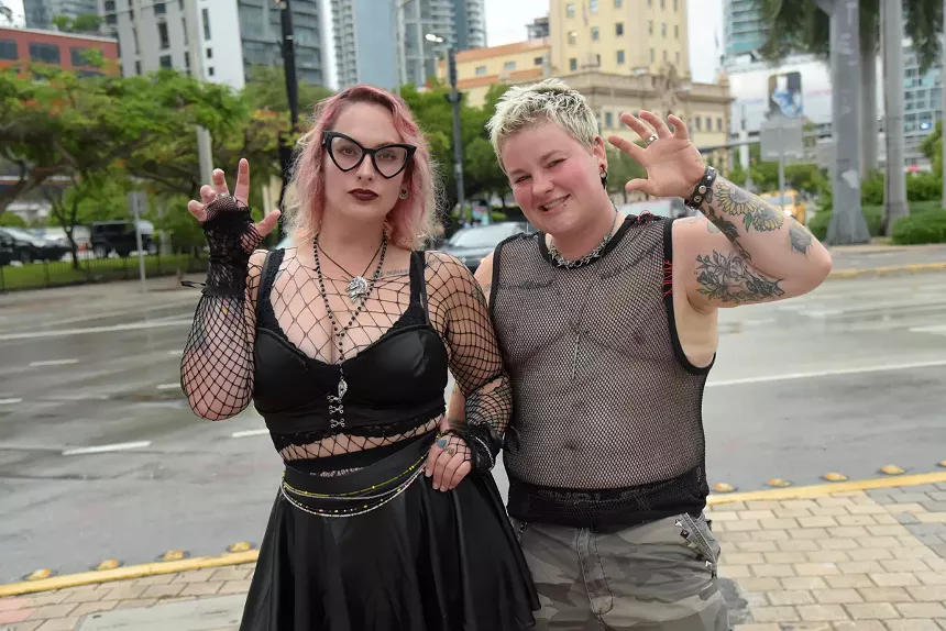 Two people in black leather and mesh outfits pose for a photographer forming claws with their hands