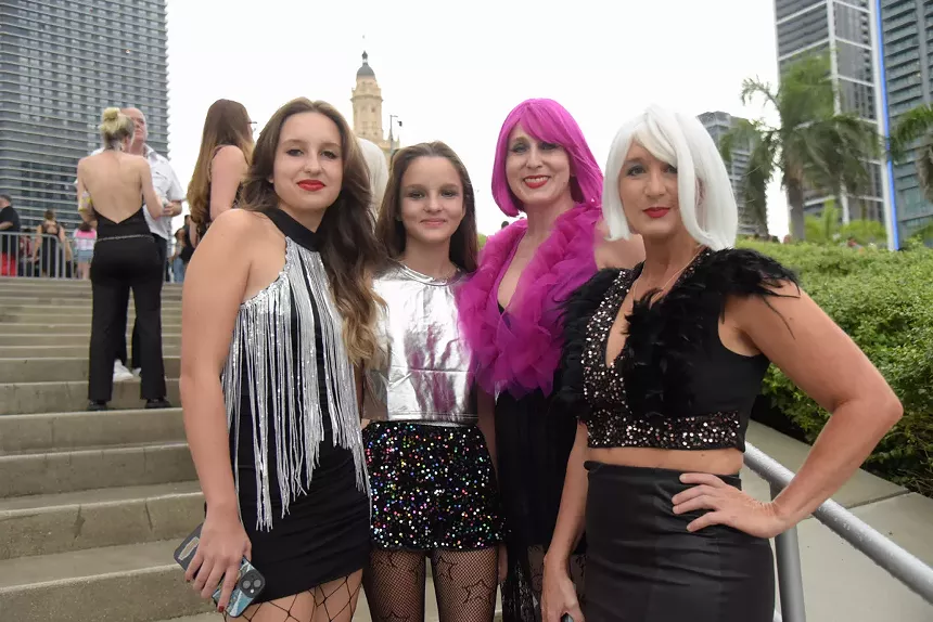 four women and girls in glittered and fringed outfits, and colorful wigs