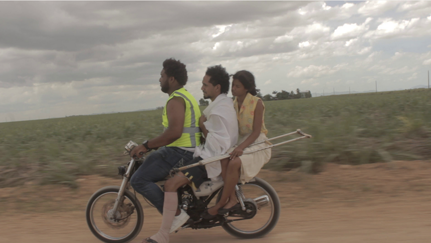 three people ride a motorized bicycle in the countryside