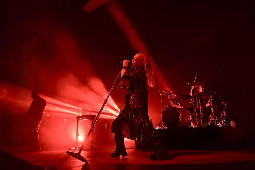 Picture of a singer on stage holding a microphone under red lights.