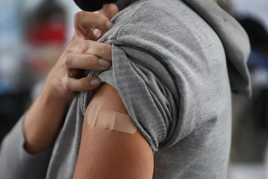 Someone wearing a grey sweater lifts the sleeve to reveal a bandage.