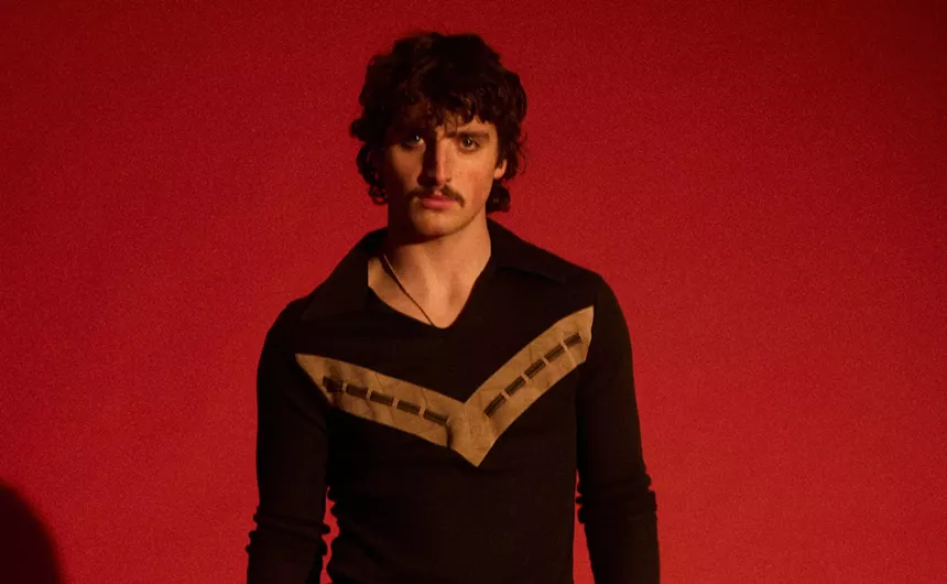 portrait of singer Benson Boone in front of a red background