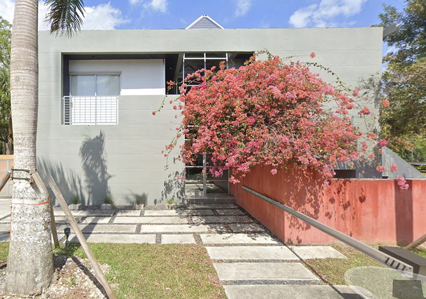 a boxy cement house with a bougainvillea bush in front