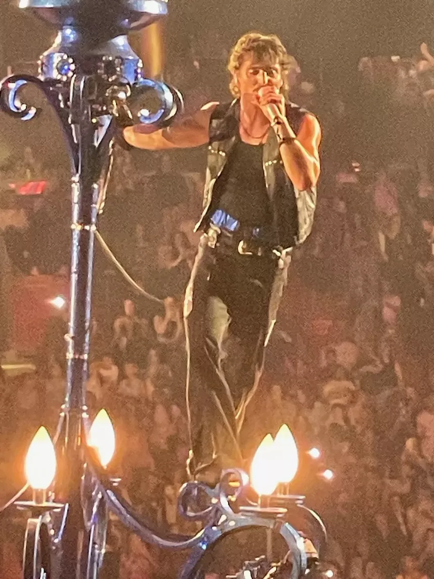 Picture of Benson Boone singing on top of a chandelier.