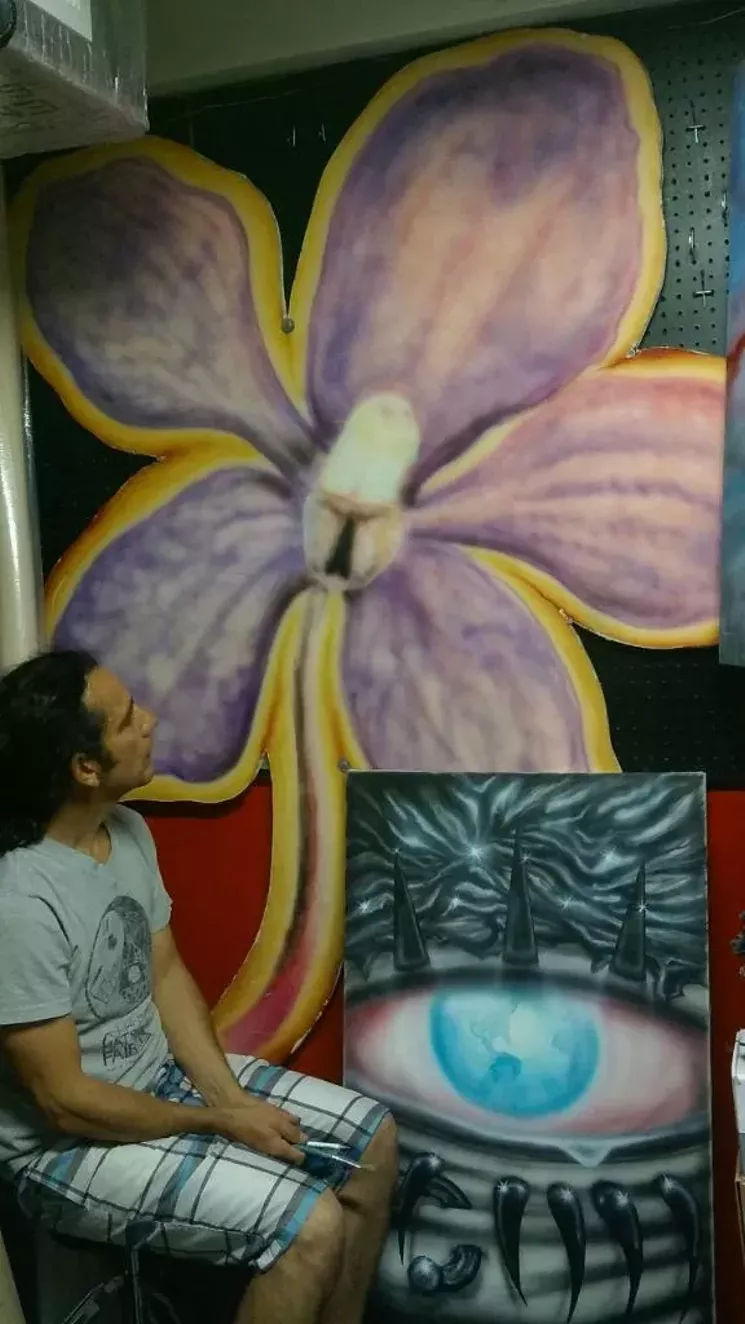 Wallflower alumnus Anibal Fernandez with the flower logo he painted on a chunk of drywall at the original gallery. - COURTESY OF ANIBAL FERNANDEZ