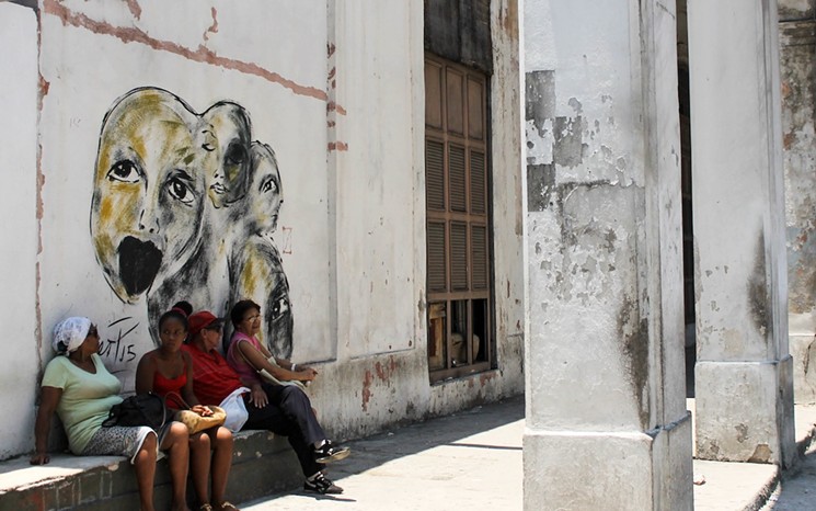 Havana dwellers sit beneath one of Pérez's murals. - ANGELA GERVASI