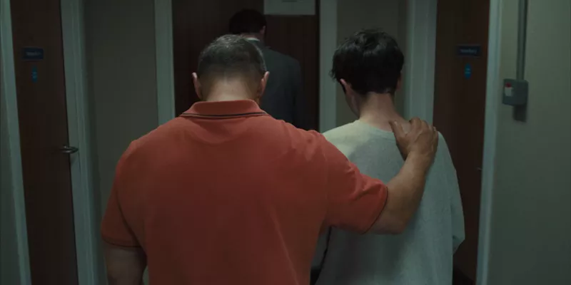 Image: still from the Netflix show Adolescence. An adult man puts his arm around a young man