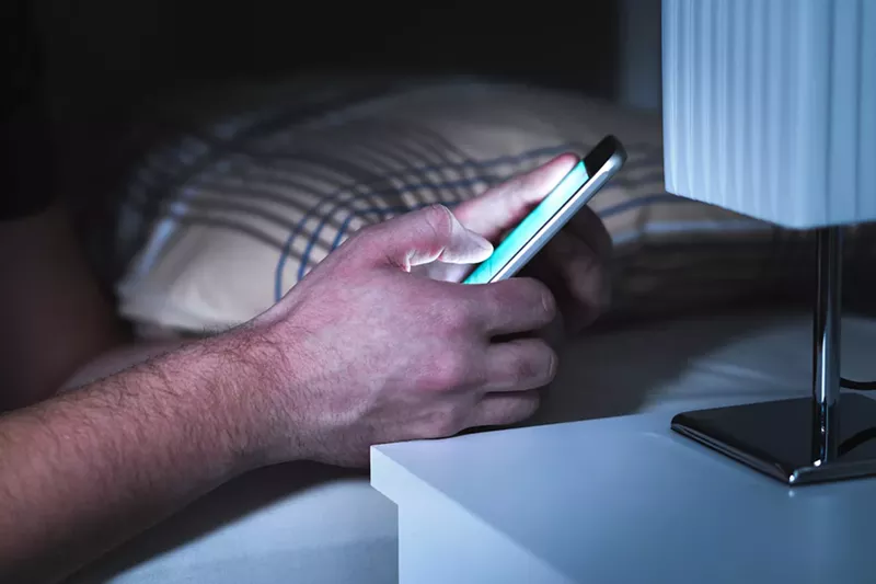 Image: closeup of a man's hand texting in bed