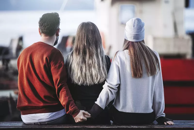 Image: A man and woman holding hands behind another woman