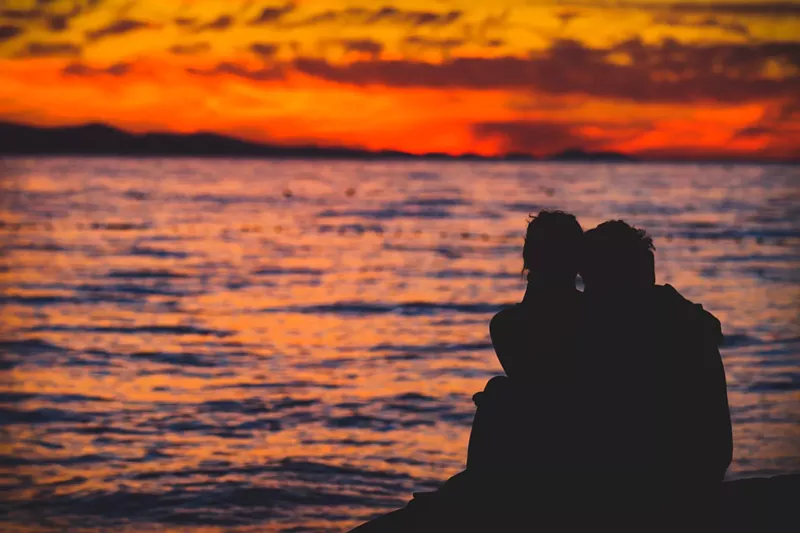 Image: a couple in silhouette looks out at the ocean during golden hour