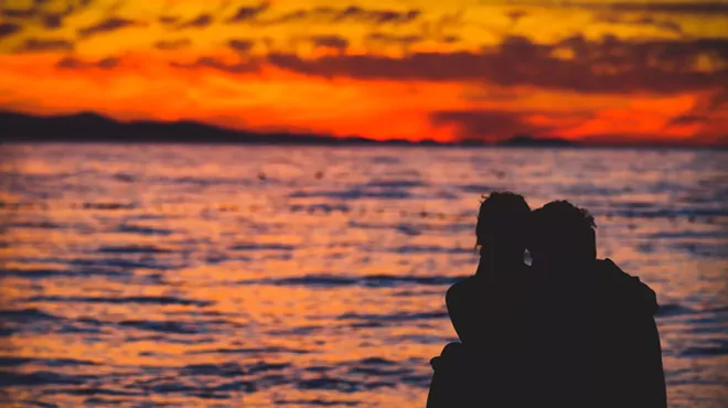 a couple in silhouette looks out at the ocean during golden hour