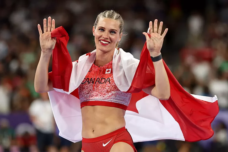 Image: Pole vaulting champion Alysha Newman, wearing cornrolls in her hair and draped in the Canadian flag, waves during the Paris Olympics