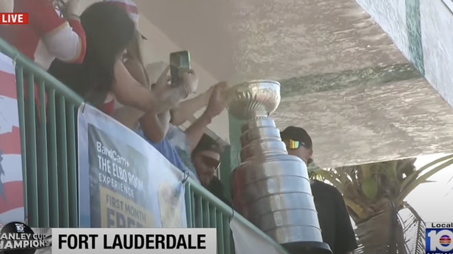 Florida Panthers players hold the Stanley Cup on a balcony, surrounded by fans