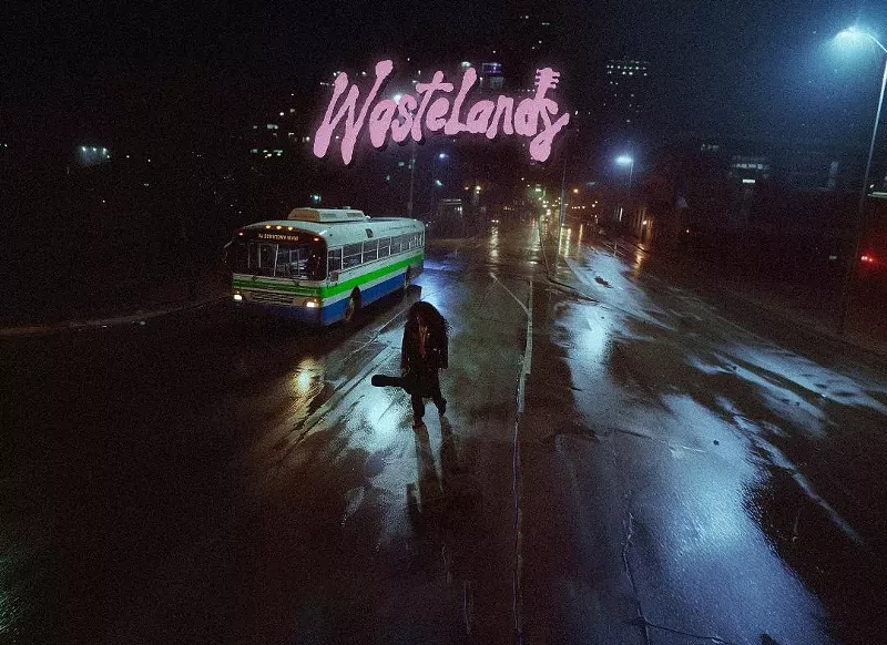 Image: Image of a man walking at night carrying a guitar.