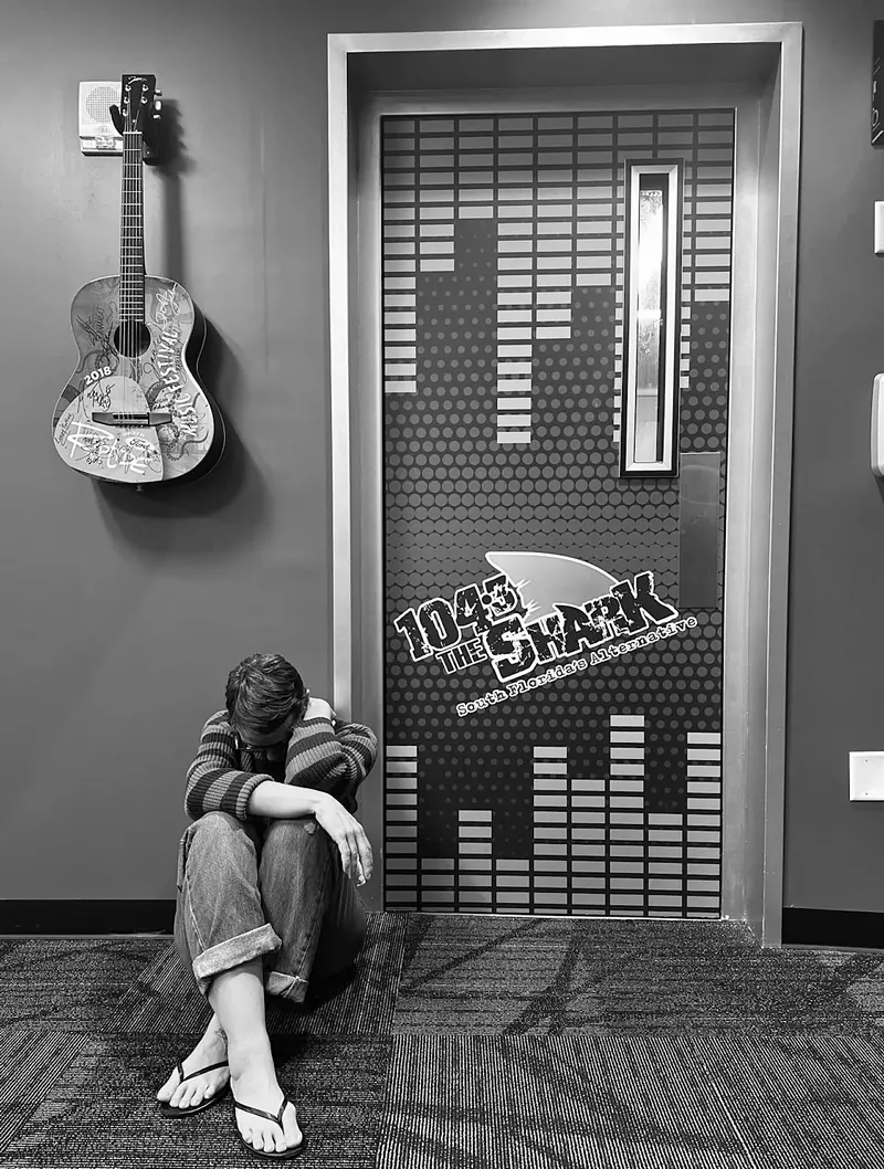 Image: A woman sitting by a door outside a radio station