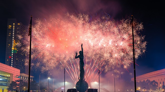A large cluster of fireworks explode with a statue silhouette in the foreground in Cleveland