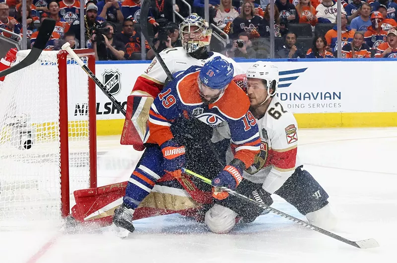 Image: A Panthers player ties up an Edmonton Oilers skater at the Panthers net in the Stanley Cup Finals as ice sprays into the air