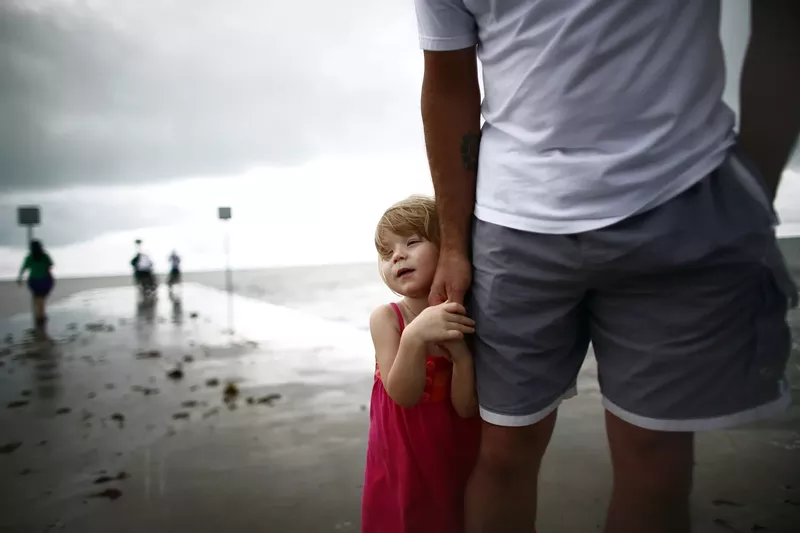 Image: a small child in a red dress holding a man's hand on a beach in the Florida Keys on a stormy day