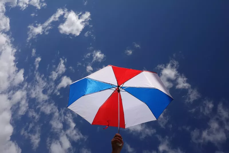 Image: A red, white, and blue umbrella held up against a mostly clear sky with scattered clouds