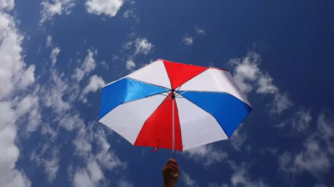 A red, white, and blue umbrella held up against a mostly clear sky with scattered clouds