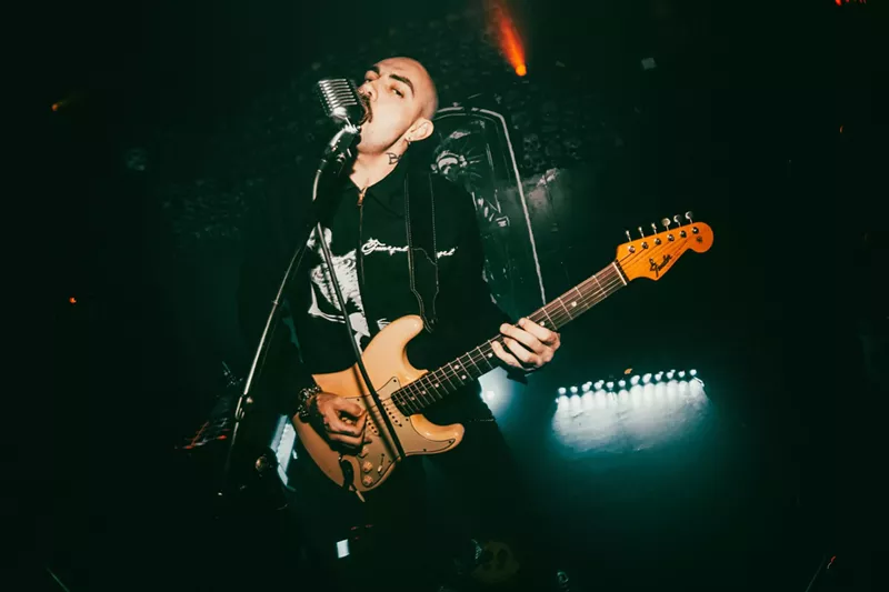 Image: Miami musician Niko Javan singing into a microphone and strumming his guitar, performing as Blood Orchid