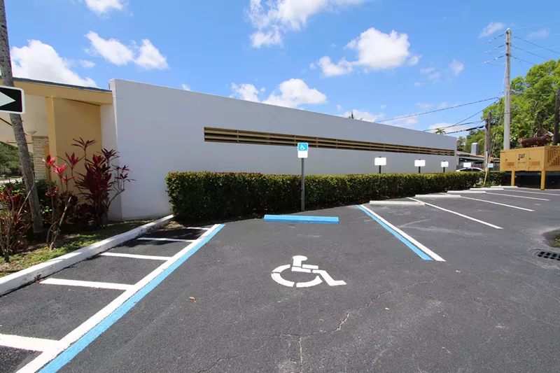 Image: A set disabled parking lot spaces in front of a city hall building, with blue skies in background