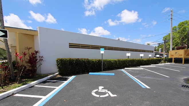 A set disabled parking lot spaces in front of a city hall building, with blue skies in background